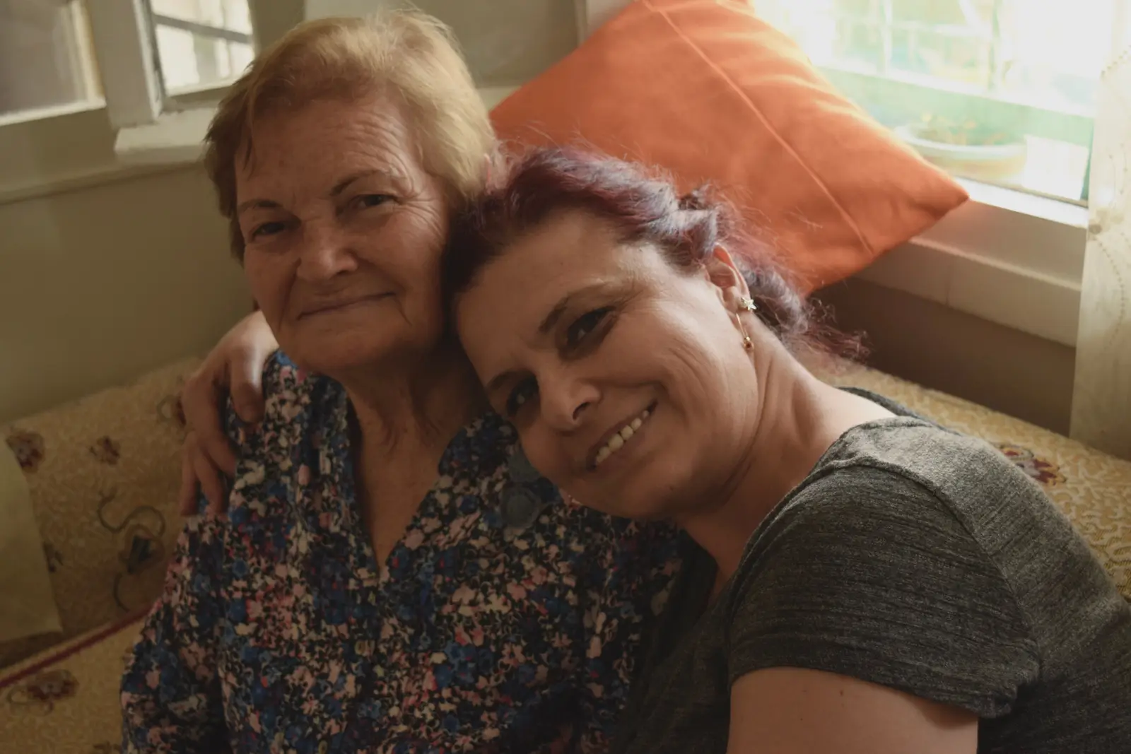 A grown daughter hugs her smiling elderly mother at home